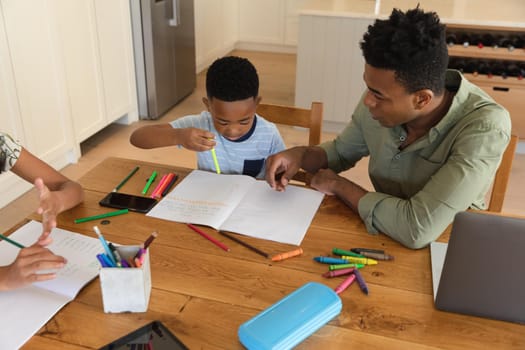 Happy african american father with daughter and son doing homework at home smiling. family domestic life, spending time working together at home.