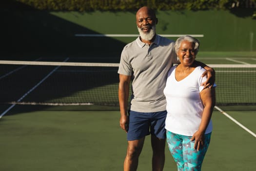 Portrait of smiling senior african american couple embracing on tennis court. retirement and active senior lifestyle concept.