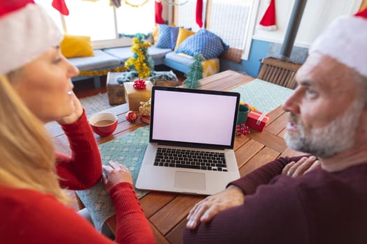 Happy caucasian mature couple making a video call and using laptop with copy space. christmas, festivity and communication technology.