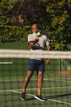 Senior african american man playing tennis striking ball on tennis court. retirement and active senior lifestyle concept.