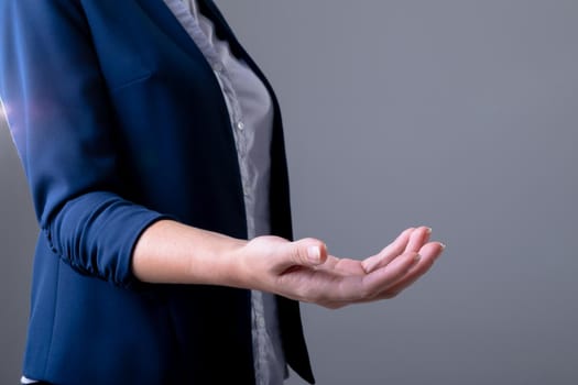 Midsection of caucasian businesswoman reaching with her hand, isolated on grey background. business technology, communication and growth concept digitally generated composite image.