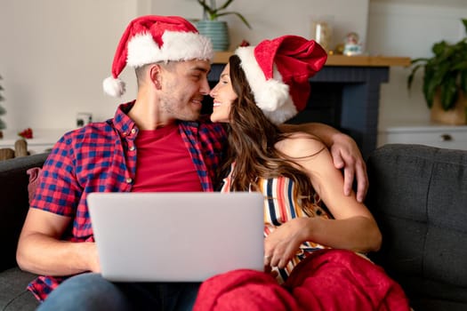 Happy caucasian couple wearing santa hats, hugging and having video call on laptop at christmas time. christmas, festivity and communication technology.