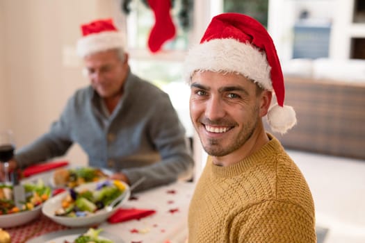 Happy caucasian man wearing santa hat looking at camera at christmas table. family christmas time and festivity together at home.