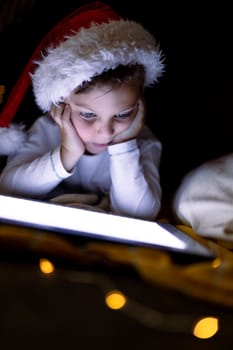 Focused caucasian boy wearing santa hat, using tablet at christmas time. childhood, chiristmas, festivity and tradition at home.