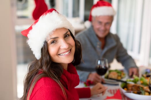 Happy caucasian woman wearing santa hat sitting at christmas table and looking at camera. family christmas time and festivity together at home.