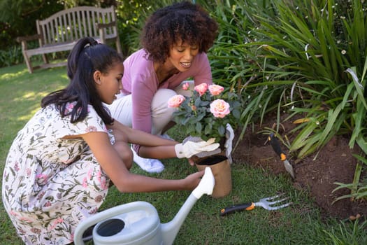 Happy african american mother with daughter outdoors, gardening on sunny day. family enjoying quality free time together.