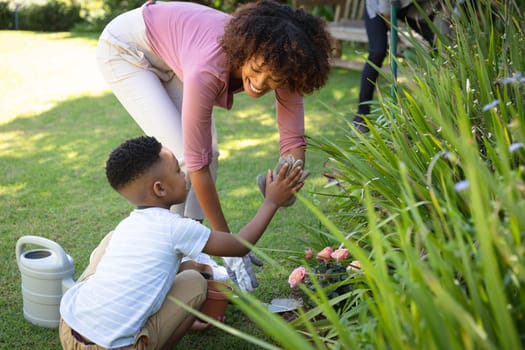 Happy african american mother with son outdoors, gardening on sunny day. family enjoying quality free time together.