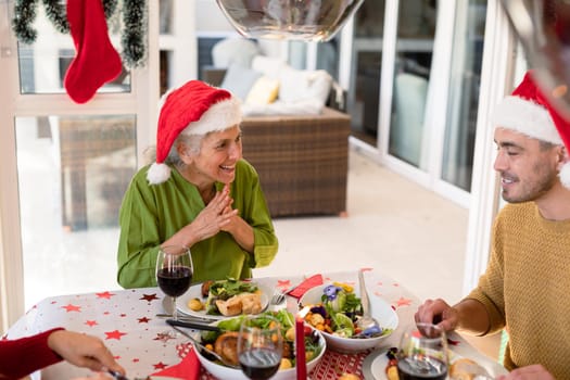 Happy caucasian adult son and senior mother wearing santa hats sitting at christmas table. family christmas time and festivity together at home.