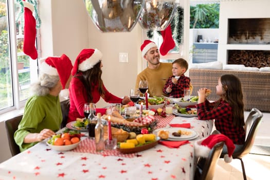 Caucasian multi generation family wearing santa hats having christmas meal. family christmas time and festivity together at home.