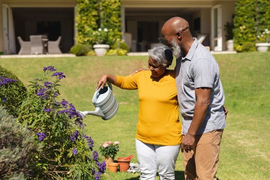 Senior african american couple spending time in sunny garden together watering flowers. retreat, retirement and happy senior lifestyle concept.