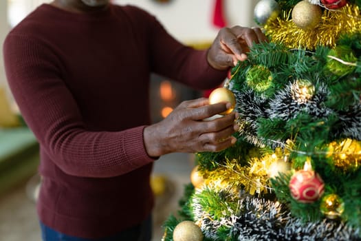 Midsection of african american senior man decorating christmas tree. retirement lifestyle and christmas festivities, celebrating at home.