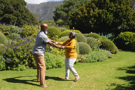 Senior african american couple spending time in sunny garden together dancing. retreat, retirement and happy senior lifestyle concept.