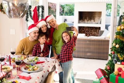 Caucasian multi generation family wearing santa hats taking selfie at christmas time. family christmas time and festivity together at home.