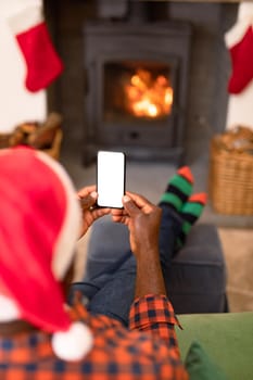 Back view of african american senior man using smartphone with copy space at christmas time. retirement lifestyle, christmas festivities and communication technology.