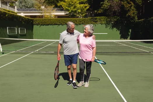 Senior caucasian couple embracing and smiling on tennis court. retirement retreat and active senior lifestyle concept.