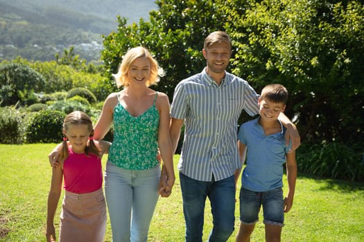 Happy caucasian couple with daughter and son outdoors, walking in sunny garden. family enjoying quality free time together.