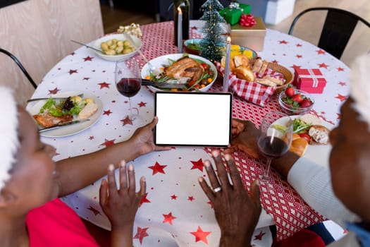 Back view of african american senior couple using tablet with copy space at christmas time. retirement lifestyle, christmas festivities and communication technology.