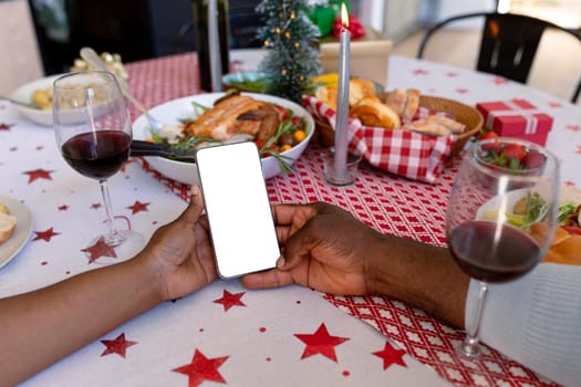 Hands of african american senior couple using smartphone with copy space at christmas time. retirement lifestyle, christmas festivities and communication technology.