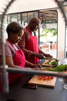 Happy african american senior couple cooking together in kitchen. retirement lifestyle, leisure and spending time at home.