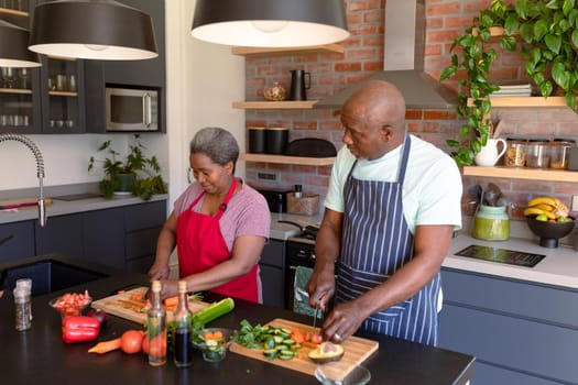 Happy african american senior couple cooking together in kitchen. retirement lifestyle, leisure and spending time at home.