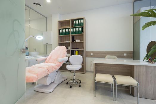 Beautiful interior of new salon, spa room, beauty parlour, or dermatological clinic with empty bed and modern skin care products on shelves and wall racks