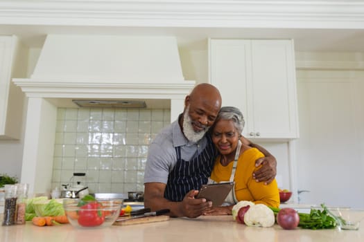 Senior african american couple cooking together in kitchen using tablet. retreat, retirement and happy senior lifestyle concept.