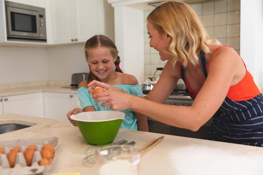 Caucasian mother and daughter baking and smiling in kitchen. family enjoying quality free time preparing food together.