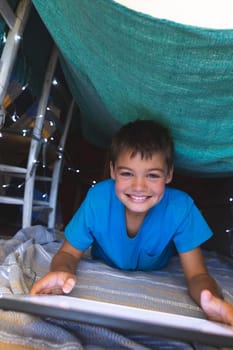 Portrait of caucasian boy smiling, lying in blanket fort using tablet at home. childhood with technology, spending free time at home.