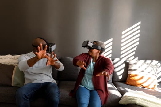 Happy african american senior couple wearing vr headset and having fun at home. retirement lifestyle, technology and spending time at home.