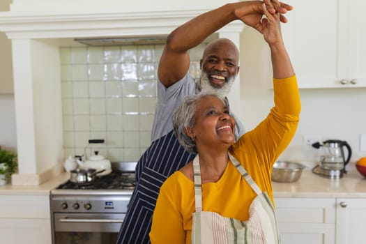 Senior african american couple dancing together in kitchen smiling. retreat, retirement and happy senior lifestyle concept.