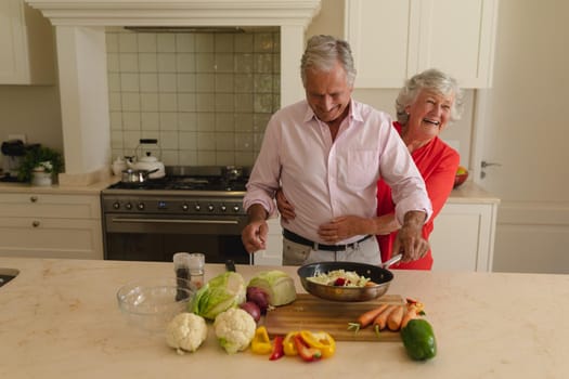 Senior caucasian couple cooking together and smiling in kitchen. retreat, retirement and happy senior lifestyle concept.