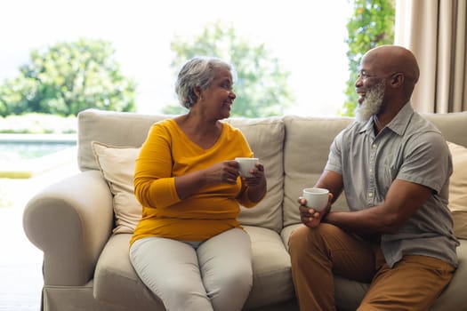 Senior african american couple sitting on sofa drinking coffee in living room. retreat, retirement and happy senior lifestyle concept.