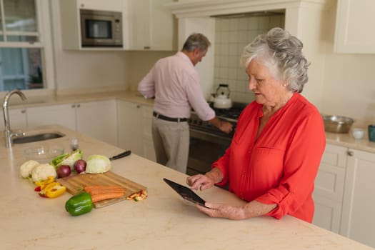 Senior caucasian couple cooking together and using tablet in kitchen. retreat, retirement and happy senior lifestyle concept.