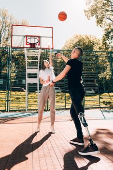 Young man with prosthetic leg playing basketball with his friend at a court.