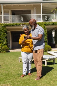 Senior african american couple spending time in sunny garden together using smartphone and smiling. retreat, retirement and happy senior lifestyle concept.