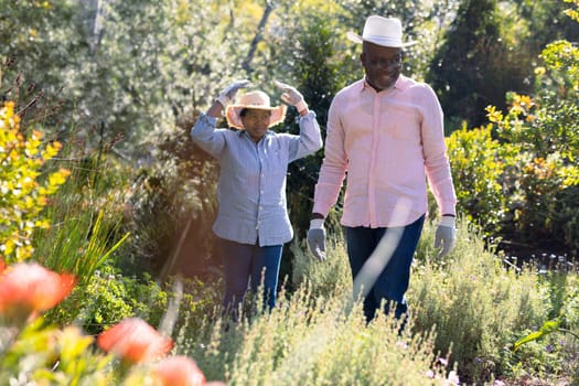 Happy african american senior couple wearing hats, gardening outdoors. retirement lifestyle, spending time at home and garden.