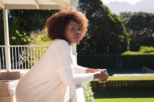 Happy african american woman relaxing on sunny balcony of country home enjoying the view. domestic lifestyle, enjoying leisure time at home.