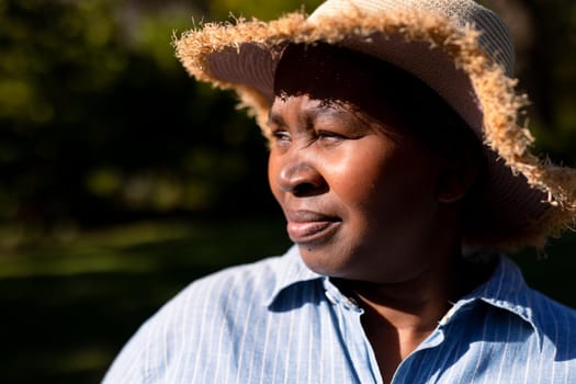 Portrait of african american senior woman wearing hat, looking into distance outdoors. retirement lifestyle, spending time at home and garden.