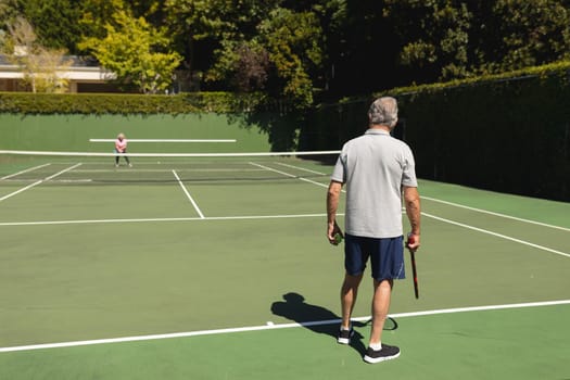 Senior caucasian couple playing tennis together on court. retirement retreat and active senior lifestyle concept.