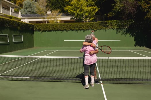 Senior caucasian couple playing tennis together on court embracing. retirement retreat and active senior lifestyle concept.