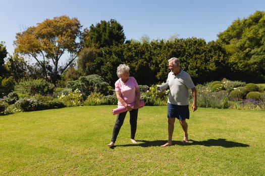 Senior caucasian couple holding yoga mats and smiling in sunny garden. retirement retreat and active senior lifestyle concept.