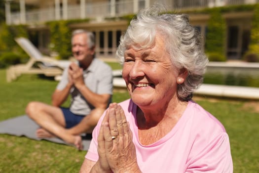 Senior caucasian couple practicing yoga, meditating in sunny garden. retirement retreat and active senior lifestyle concept.