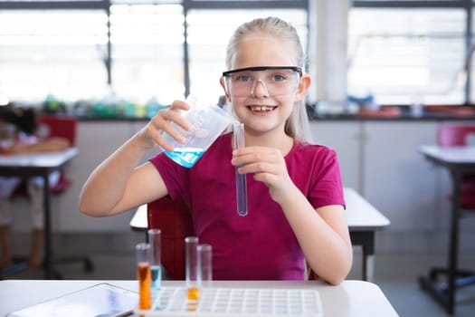 Caucasian girl pouring chemical from beaker into test tube in science class at laboratory. school and education concept