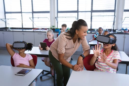 African american female teacher teaching a girl to use vr headset in the class at school. school and education concept