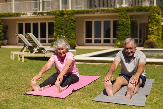 Portrait of senior caucasian couple practicing yoga, stretching in sunny garden. retirement retreat and active senior lifestyle concept.