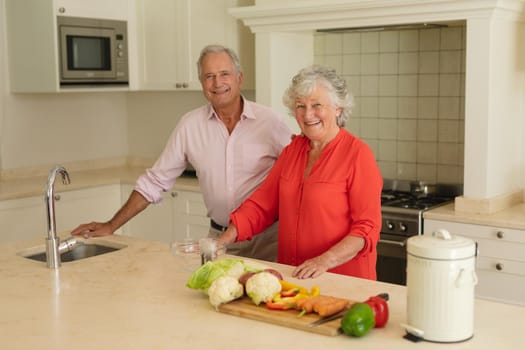 Portrait of senior caucasian couple looking at camera and smiling in kitchen. retreat, retirement and happy senior lifestyle concept.