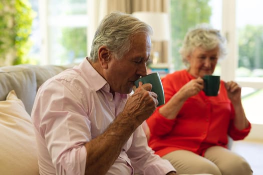 Senior caucasian couple sitting on sofa together drinking coffee in living room. retreat, retirement and happy senior lifestyle concept.