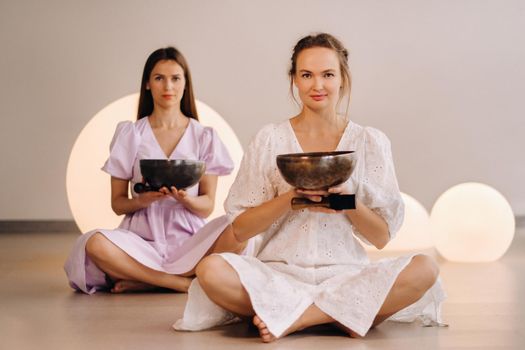 Two female yoga teachers playing a Tibetan bowl in the gym during a yoga retreat.