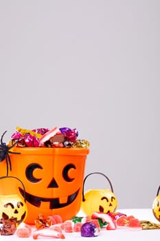 Composition of halloween bucket with trick or treat sweets, spider and pumpkins on white background. halloween tradition and celebration concept.
