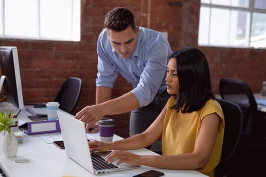 Caucasian male and female business colleague looking at laptop and discussing at desk in office. working in business at a modern office.